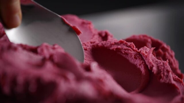 Cinematic close-up of a gelato artisan shaping ice cream with a spatula. The tool reveals creamy texture and smooth movement in soft dramatic lighting.