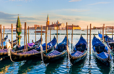 Fototapeta premium row of parked venetian gondola boats in Grand canal of Venice. Beautiful sunset or sunrise landscape with gondolas in blue water of Venice.