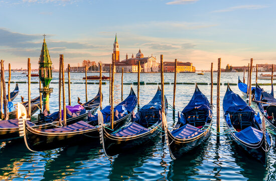row of parked venetian gondola boats in Grand canal of Venice. Beautiful sunset or sunrise landscape with gondolas in blue water of Venice.