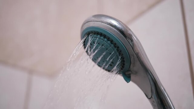 Water flows from a shower head against a tiled background, perfect for lifestyle, relaxation, and hygiene-related projects.