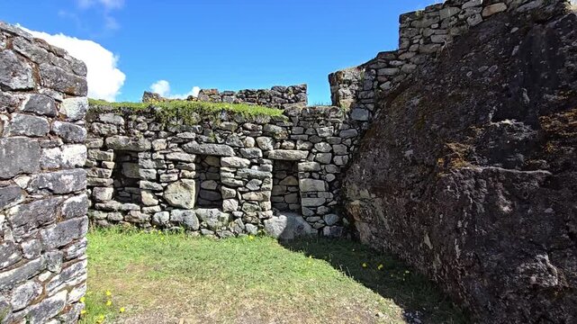Sayacmarca, Peru - 26 June 2024. Inca ruins with stone walls integrated around a large natural rock outcrop, set on a grassy terrace along the Inca Trail in the Andes.