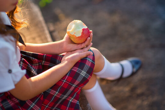 Schoolgirl sitting outdoors and holding a bitten red apple in her hands