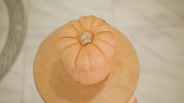 Overhead mini pumpkin on wooden stool, soft warm light, marble floor backdrop, textured stem detail, studio still life composition, seasonal decor, baker inspiration for pumpkin pie, recipe imagery,