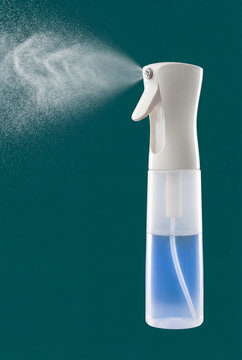 White plastic spray bottle dispensing mist against teal background