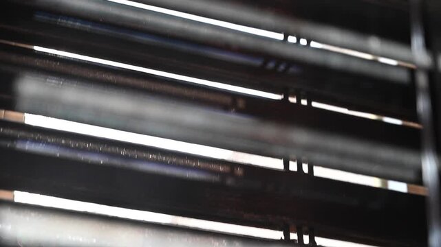 Close-up video of window shutters opening in the morning, allowing soft beams of sunlight to filter into the room. Backlit scene with warm tones and gentle shadows, ideal for themes of daily routine, 
