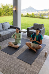Fototapeta premium Couple meditating cross-legged on patio wearing activewear on yoga mats with water bottles