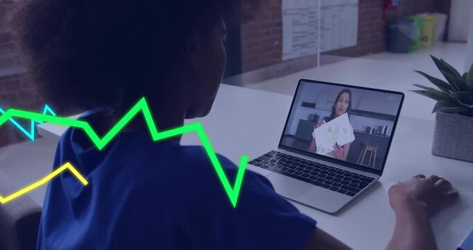 Student sitting at desk viewing laptop as host lifting papers, graphs crossing screen for teaching