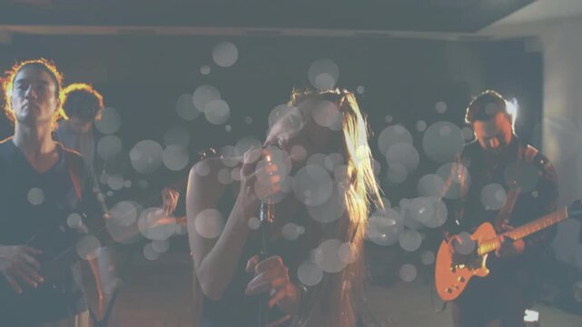 Female singer whipping hair gripping mic stand while band rehearsing, bokeh discs appearing onstage