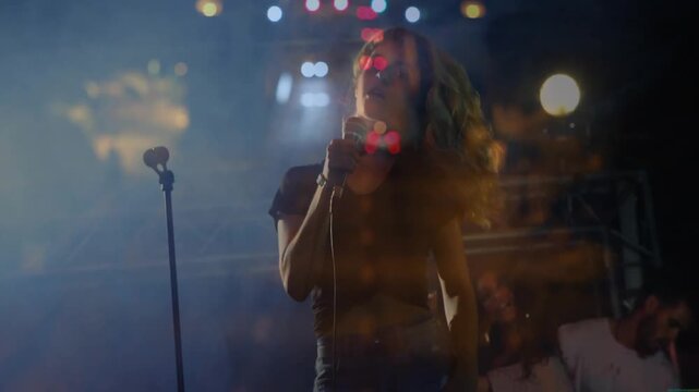 Lead singer reacting to beat, singing into mic, guitar and pulsing music lights creating bokeh haze
