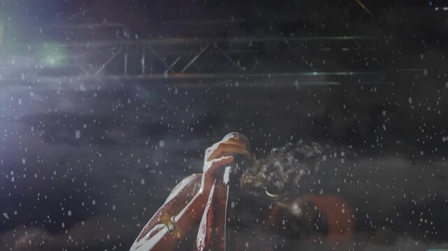 Female singer gripping mic exhaling and projecting power spraying mist whipping hair during concert