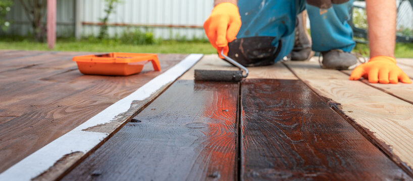 Worker applies dark finish to wooden deck surface