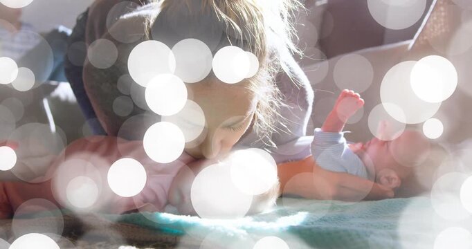 Leaning mother kissing and soothing twins at home with turquoise blanket, pink-blue onesies, bokeh