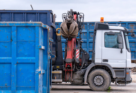 Industrial truck with boom crane and material handler grapple moving blue skip containers