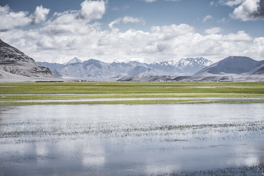 Panorama in the Tien Shan Mountains with a high plateau and rocky mountains, with a lake in the foreground, reflecting the mountain peaks and clouds, for the background