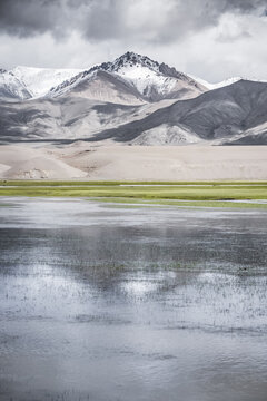 Panorama in the Tien Shan Mountains with a high plateau and rocky mountains, with a lake in the foreground, reflecting the mountain peaks and clouds, for the background