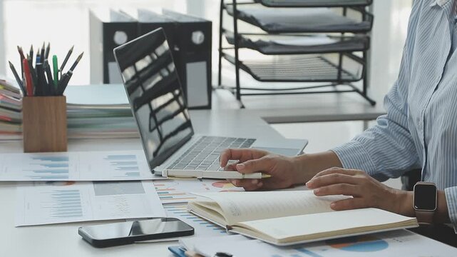 Close up of businessman or accountant hand holding pen working on calculator to calculate business data, accountancy document and laptop computer at office, business concept