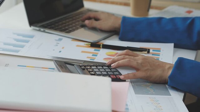 Close up of businessman or accountant hand holding pen working on calculator to calculate business data, accountancy document and laptop computer at office, business concept