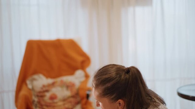 Woman and child decorating pumpkin craft. Cozy kitchen light, orange throw on chair, markers on small table, mother teaching daughter to draw friendly face on gourd, warm laughter and close bonding,