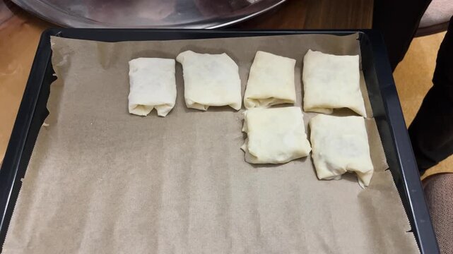 Handmade b&ouml;rek arranged on a baking sheet; the process of preparing this delicious pastry from traditional Turkish cuisine and its presentation.