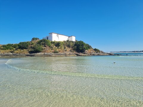 Praia do Forte in Cabo Frio: crystal-clear beach, blue sky, sunny day, with the historic Fort S&atilde;o Mateus on the hill by the water. A perfect scene for relaxation and mindfulness.