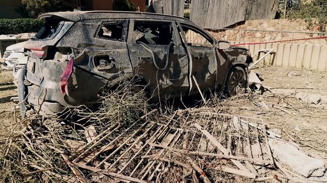 A completely smashed and destroyed car, with broken windows and splashes of mud, standing in a parking lot next to a heavy missile falling site, during the Israel Iran war. Arad, Israel.