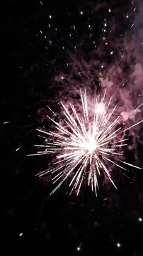 Vertical video looking up at New Year's fireworks. Fireworks exploding in bright colors at night, a tradition for celebrating the start of a new year and the end of the old as the clock strikes 12.