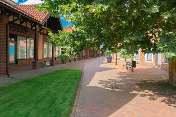 Obraz premium Empty pedestrian walkway in modern european town with beautiful red brick architecture and green lawn under blue sky. Summer city landscape