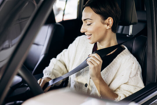 Woman sitting inside a new car and fastening seat belt in a dealership showroom. Customer testing vehicle interior before purchase, buckling up safety belt