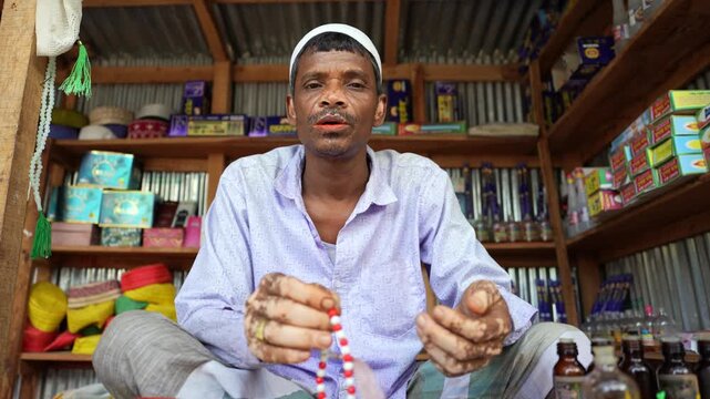 Street shopkeeper in northern Bangladesh quietly counts rosary beads while seated in his small shop, his vitiligo marked face glowing with calm dignity in a warm, portrait, leukoderma , leucoderma