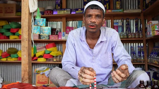 Street shopkeeper in northern Bangladesh quietly counts rosary beads while seated in his small shop, his vitiligo marked face glowing with calm dignity in a warm, portrait, leukoderma , leucoderma