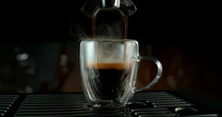 Fresh espresso pouring from coffee machine into glass cup with rich crema and rising steam. Warm cinematic scene capturing preparation of black coffee in cozy atmosphere. © Jag_cz