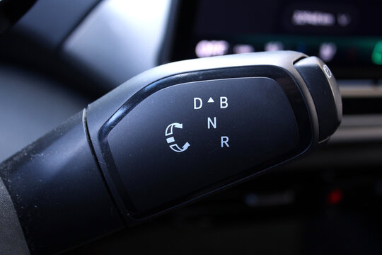 Close up black gear selector stalk displays illuminated white letters D B N R with circular arrow icon curved ergonomic shape glossy finish matte accents. Close up of the automatic gearbox lever, blac