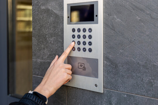 Hand pressing keypad on video intercom panel. Close-up of a hand entering a code on a modern video intercom, showing secure building access, smart entry, and safety.