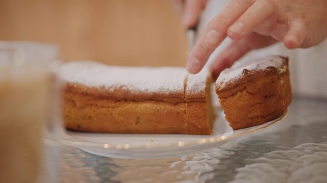Hands slicing pumpkin pie on glass plate, powdered sugar dusting, warm golden crumb revealed, closeup of knife cutting and baker lifting slice for serving, cozy kitchen table atmosphere with autumn