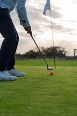 Obraz premium Golfer Preparing a Putt on Green at Sunset with Red Ball