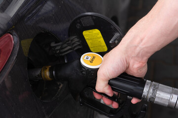 Close up of hand holding diesel pump nozzle inserted into car fuel tank, showing refueling process and transport theme
