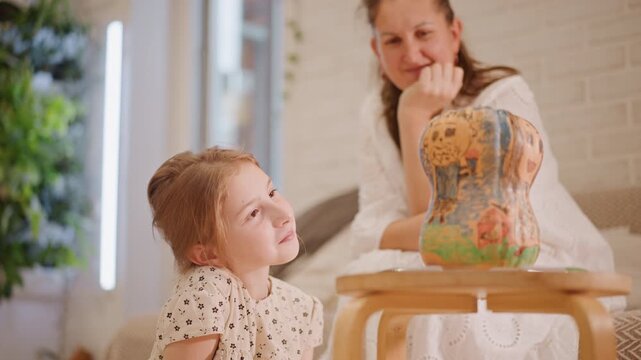 White mother watches daughter and pumpkin gourd on table, gentle forehead touch, markers scattered, mother smiling encouragement, cozy living room interior, quiet conversation and storytelling about