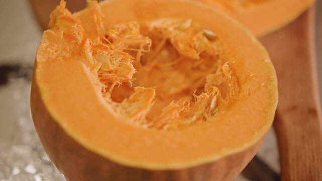 Halved pumpkin on wooden board seeds visible, warm orange flesh with stringy pulp, cavity scraped, metal foil and chopping board background, closeup texture detail, autumn harvest mood, prep