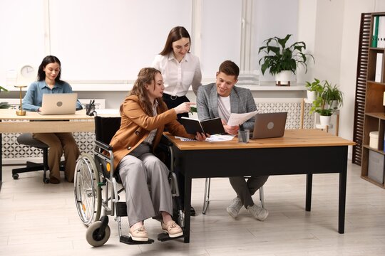 Inclusion. Woman in wheelchair and her colleagues working in office
