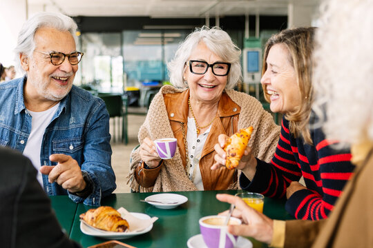Group of diverse senior friends sharing a happy breakfast moment at a cafe, drinking coffee and orange juice, enjoying croissants, and having a good time together