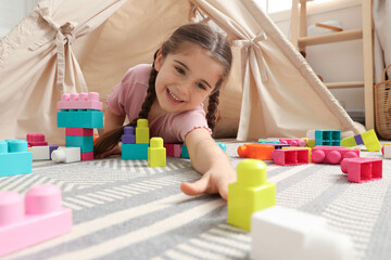 Little girl playing with building blocks near toy wigwam in playroom, low angle view © New Africa