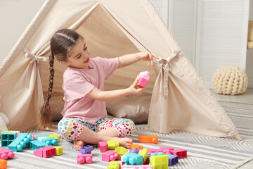Little girl playing with building blocks near toy wigwam in playroom, space for text © New Africa