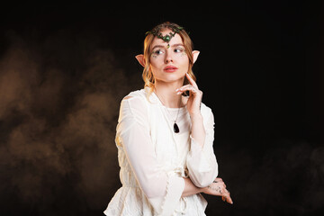 Obraz premium Beautiful girl dressed as elf on black background with smoke