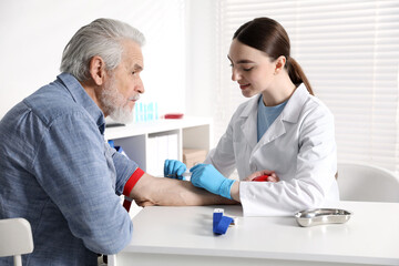 Obraz premium Doctor drawing senior man's blood sample in clinic