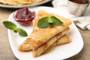 Tasty crepes with mint leaves and jam served on wooden table, closeup © New Africa