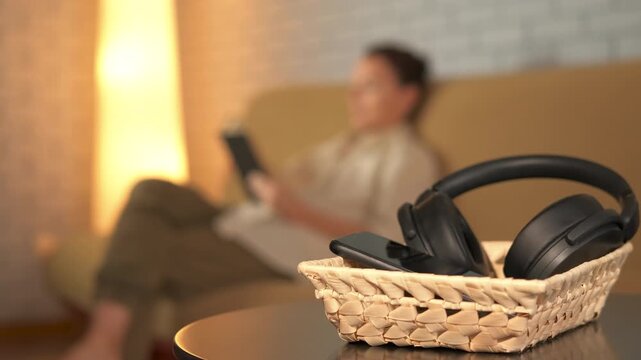 Person decluttering home office putting away gadgets. Woman putting her electronic gadgets, smartphone and headphones, in a basket on the coffee table. Concept of digital detox