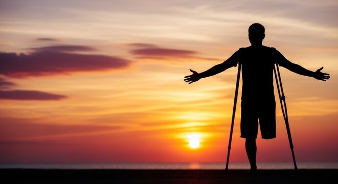 Disabled man with one leg and crutches enjoying freedom and nature during a golden sunrise.