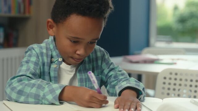 Closeup concentrated African American little boy kid child son schoolboy pupil writing homework in school kindergarten schoolchild baby write in copybook textbook elementary study education studying