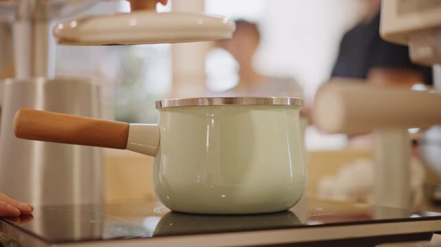 Saucepan lid placement. Soft cafe lighting illuminates pastry apprentice working carefully. Measuring tools and concentration highlighted during saucepan lid placement in professional kitchen