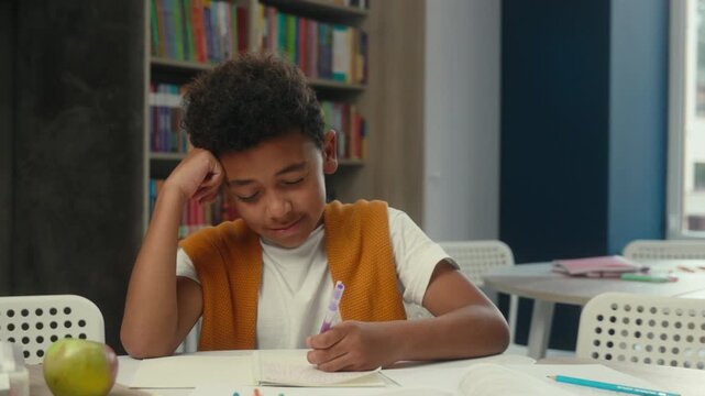 Caucasian African American boy child kid feeling tired writing homework study learn low energy rubbing eyes sleepy adorable pupil son write primary elementary studying learning task in school library